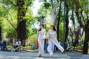 Due donne in tradizionali Ao Dai vietnamiti camminano in un viale alberato, incarnando l'incanto culturale che Cocco Travel offre nei suoi tour in Indocina.