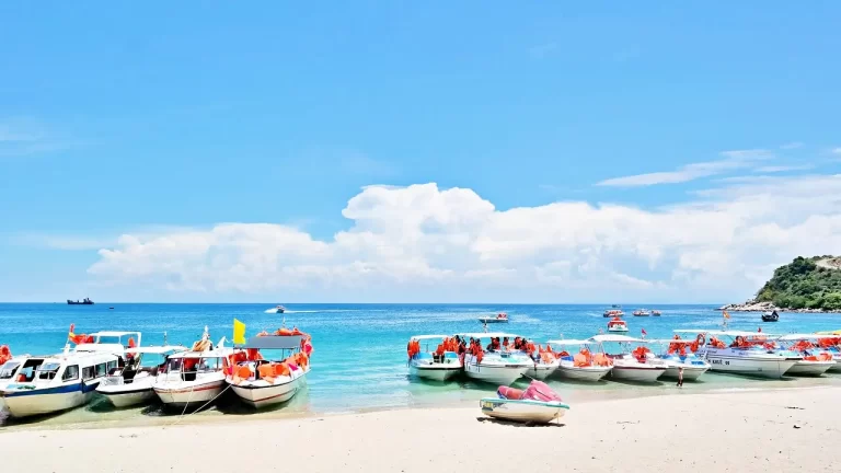 Una vivace spiaggia in Vietnam con barche allineate sulla riva e turisti che si godono attività acquatiche sotto un cielo azzurro e sereno.