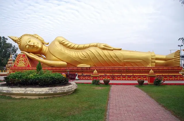 Una maestosa statua dorata del Buddha dormiente situata in un tranquillo giardino in Laos, simbolo di pace e spiritualità.