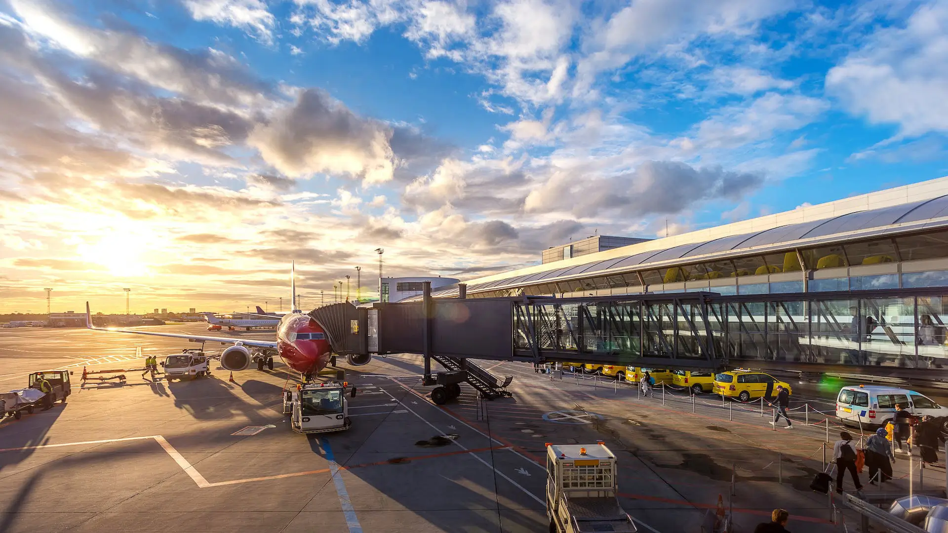 Aeroporto all'alba con un aereo collegato al gate, riflettendo i primi raggi del sole che simboleggiano l'inizio di un viaggio verso il Vietnam.