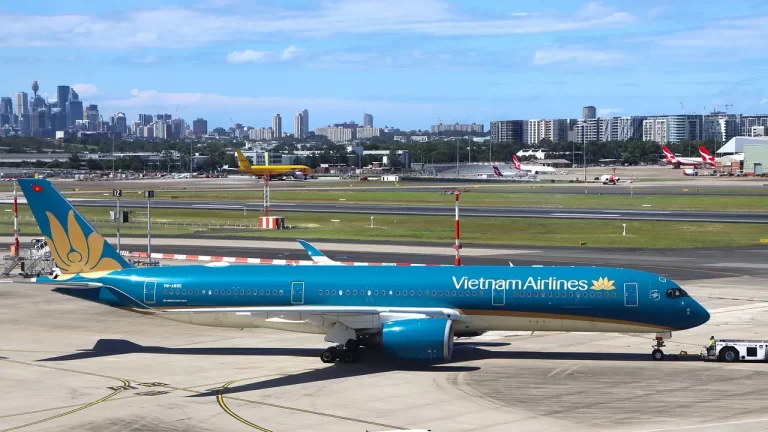 Aereo di Vietnam Airlines in sosta sul tarmac con lo skyline urbano sullo sfondo, pronto a partire per connettere i viaggiatori alle meraviglie del Vietnam.