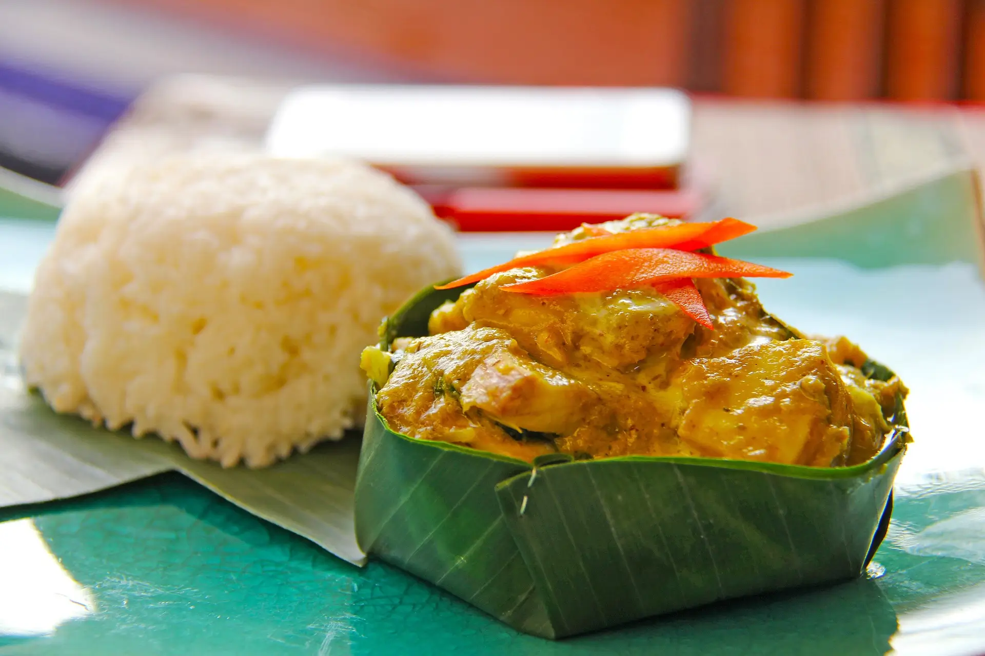 Scopri l'Amok, il celebre piatto di pesce al vapore di Battambang, incapsulato in una foglia di banano e servito con riso morbido. Questa immagine cattura l'essenza della cucina tradizionale cambogiana, riconosciuta dall'UNESCO per la sua eccezionale contribuzione alla gastronomia mondiale. Perfetta per arricchire contenuti che trattano di ricette esotiche, cultura culinaria di Battambang o per approfondimenti sulle nuove tendenze gastronomiche mondiali sostenibili e responsabili.