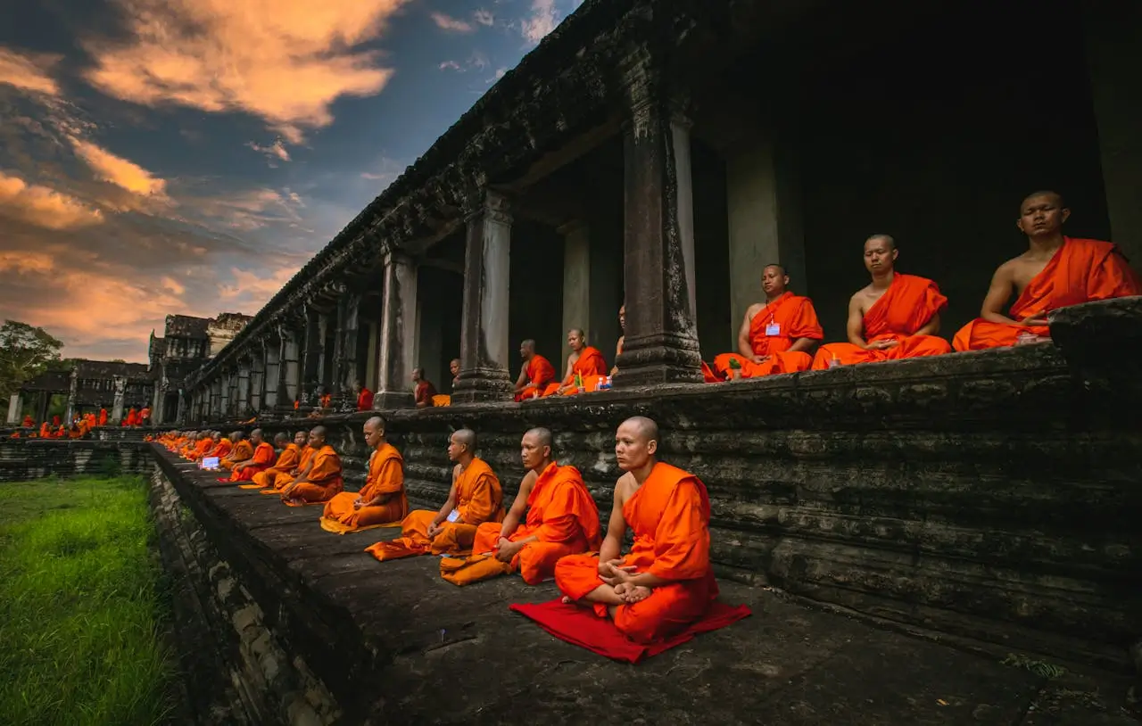 Monaci in arancione meditano in fila nel tempio di Angkor Wat, immagine iconica per rappresentare la spiritualità della Cambogia nel mese di aprile.