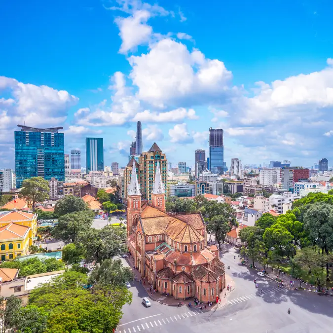 eduta aerea di Ho Chi Minh City con la Cattedrale di Notre-Dame in primo piano, esempio dell'influenza francese in Vietnam, contrasto tra storico e moderno.