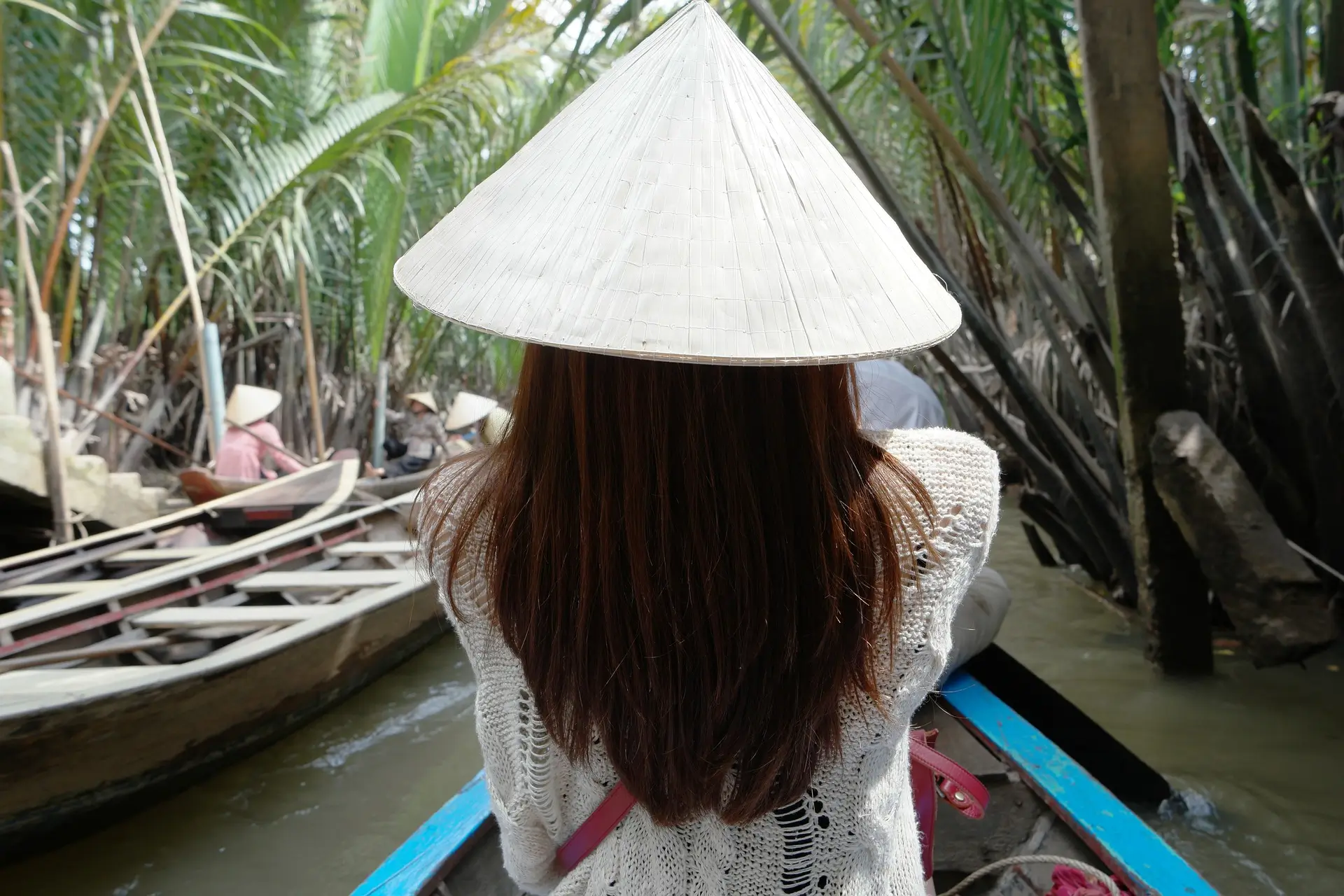 Turista donna indossa un cappello conico vietnamita mentre osserva le tipiche barche nel tranquillo Delta del Mekong, immersa nella tradizione e nella natura del Vietnam.