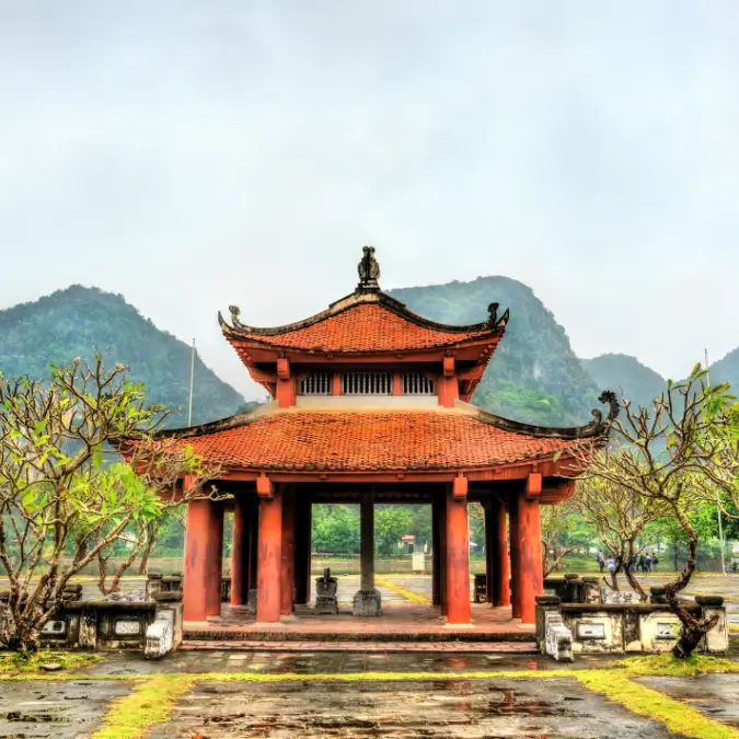 Tempio tradizionale vietnamita con tetti in stile pagoda e montagne sfocate sullo sfondo, esempio perfetto di architettura antica vietnamita a Ninh Binh, meta storica imperdibile.