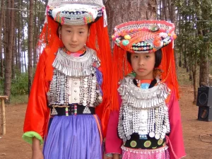 Due bambine del gruppo etnico Hmong indossano abiti tradizionali colorati in un contesto di natura.