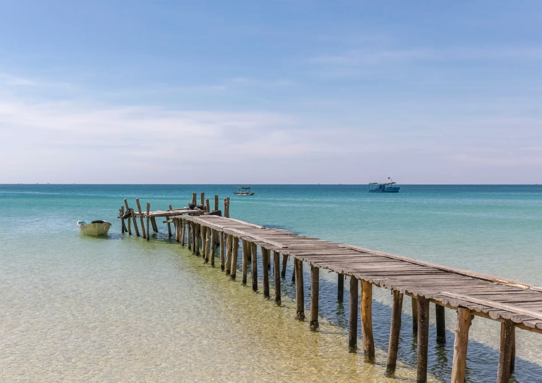 Scopri la bellezza rustica di Koh Rong con un ponte di legno che si estende verso le acque cristalline del mare in Cambogia.