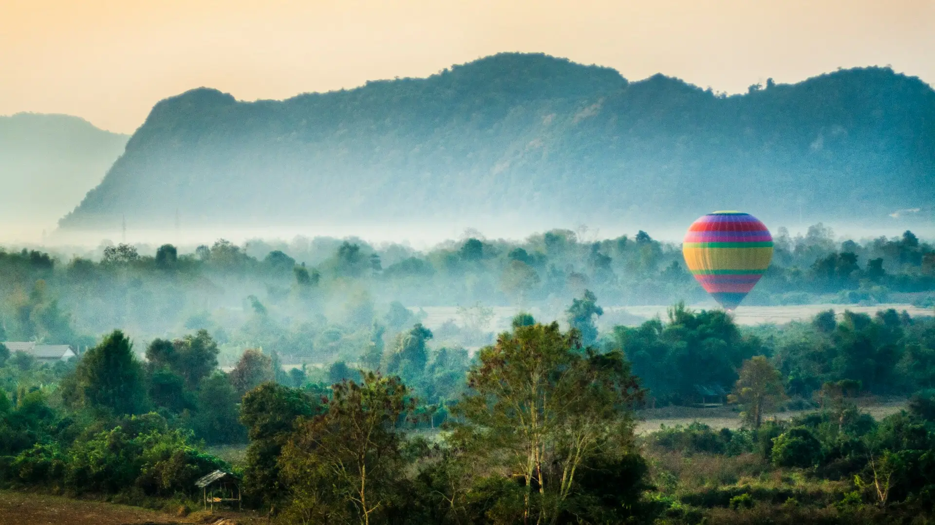 Mongolfiera colorata vola al tramonto tra le brume e il paesaggio montuoso di Vang Vieng in Laos.