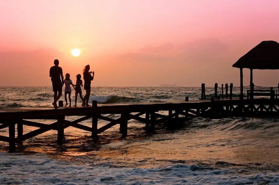 Un tranquillo momento familiare viene catturato mentre si ammira il tramonto sul Vietnam, con figure in silhouette che godono della fine di una giornata di vacanza sul pontile che si affaccia sul mare scintillante.