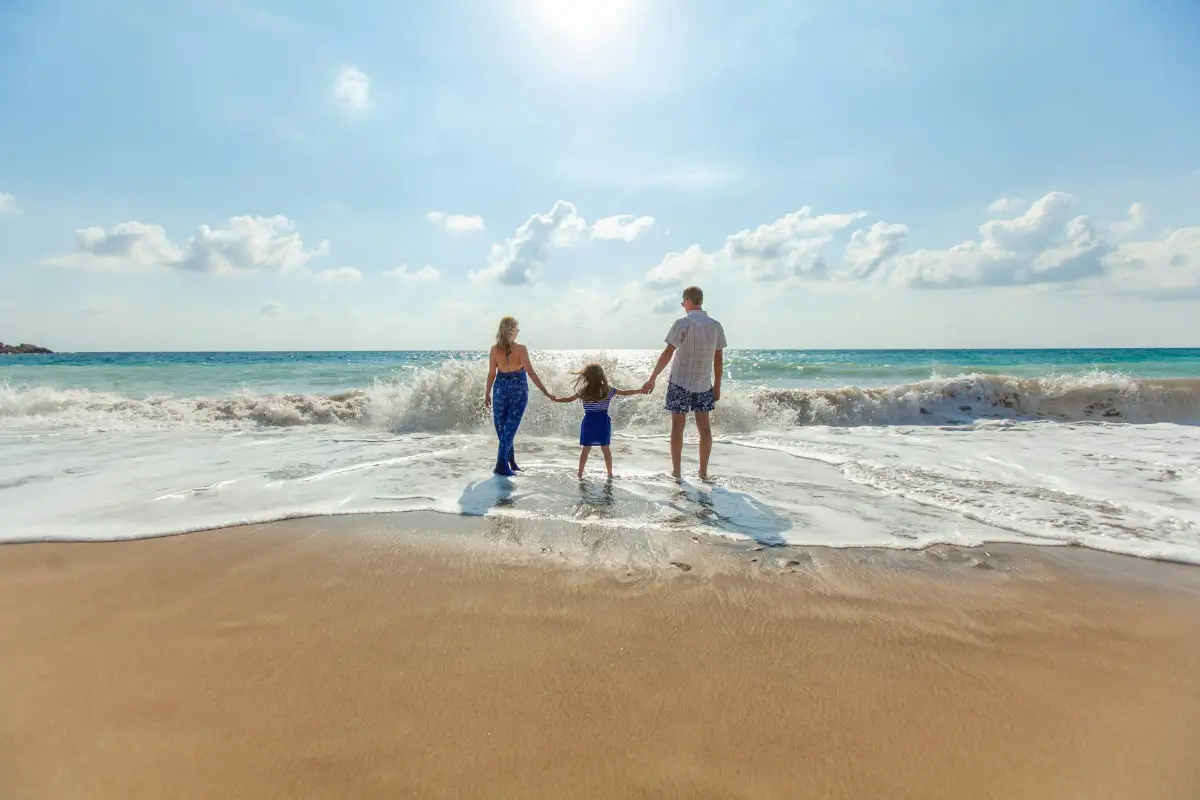 Una famiglia gioiosa si diverte con le onde sulla sabbia dorata durante la loro vacanza in Vietnam, con il mare turchese e il cielo sereno che creano un'atmosfera perfetta per le vacanze.