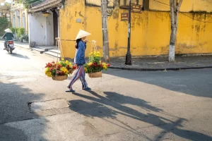 Donna vietnamita che porta fiori al mercato, indossando un cappello conico Non La.