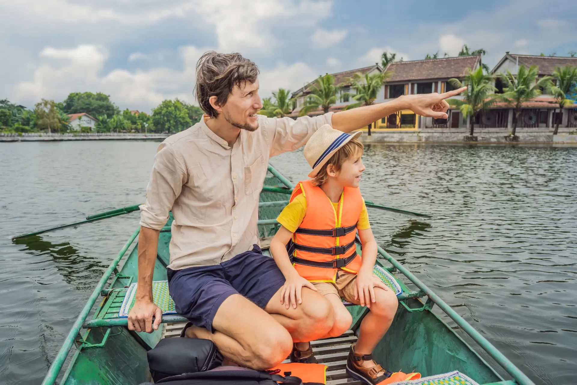 Padre e figlio che esplorano il Vietnam in barca, con il padre che indica qualcosa in lontananza e il figlio che sorride.